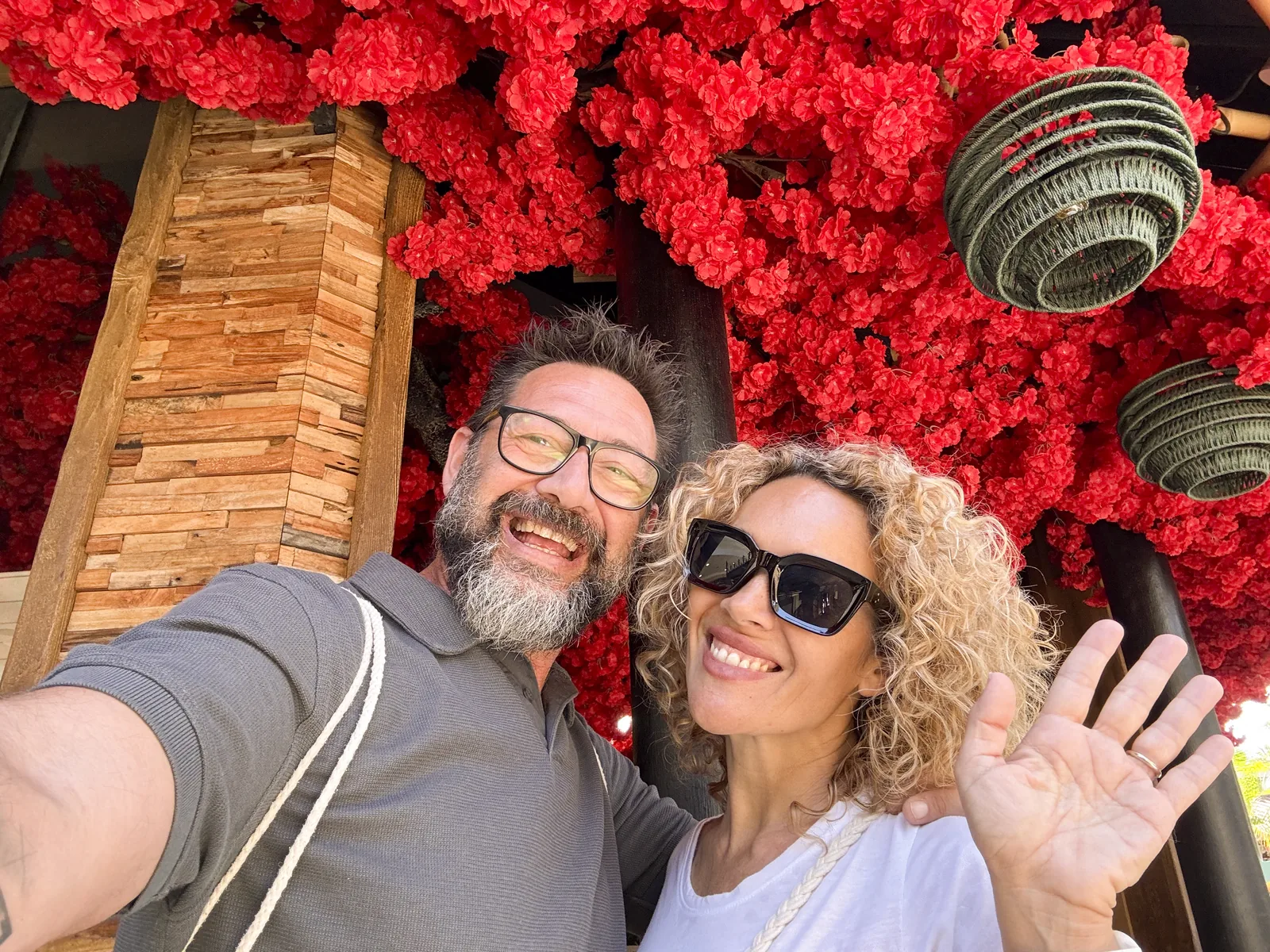 Smiling couple taking a selfie beneath a vibrant red floral display