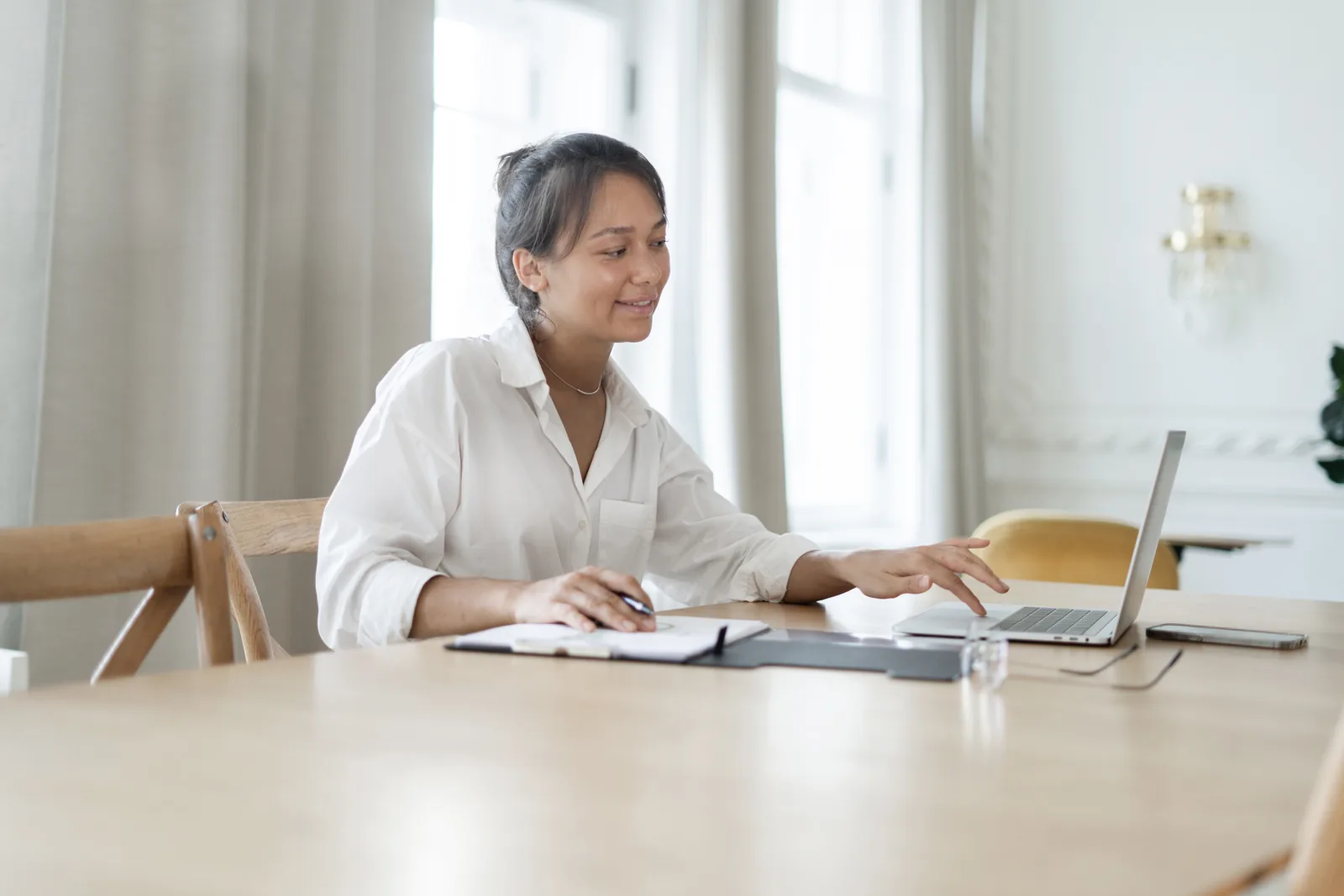 Woman using a laptop with an open notebook at a table