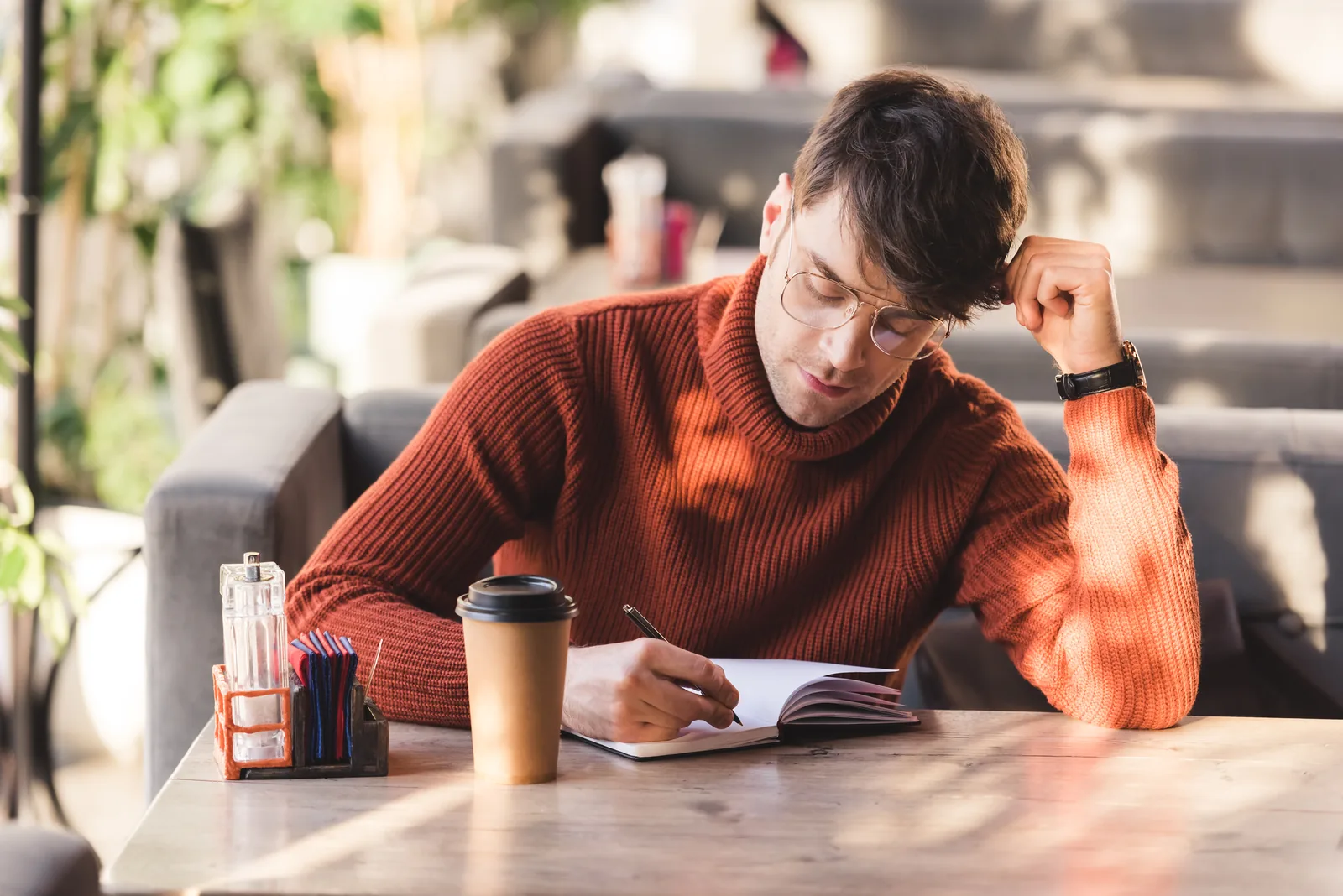 Man in an orange sweater writing in a notebook at a café table